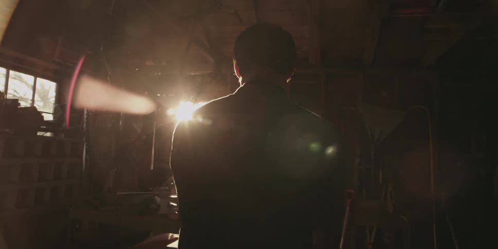 A white man stands inside a structure and looks out a door at the sun