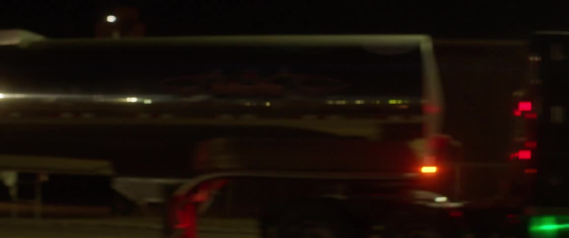 A semi-truck drives by a woman with a flashlight