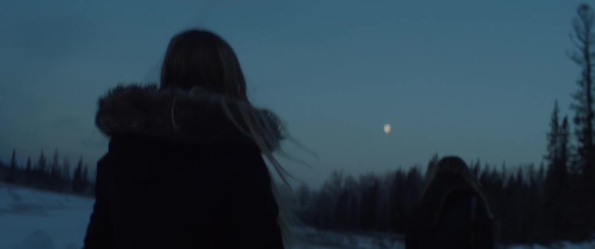 A woman walks outside at sunset in the snow