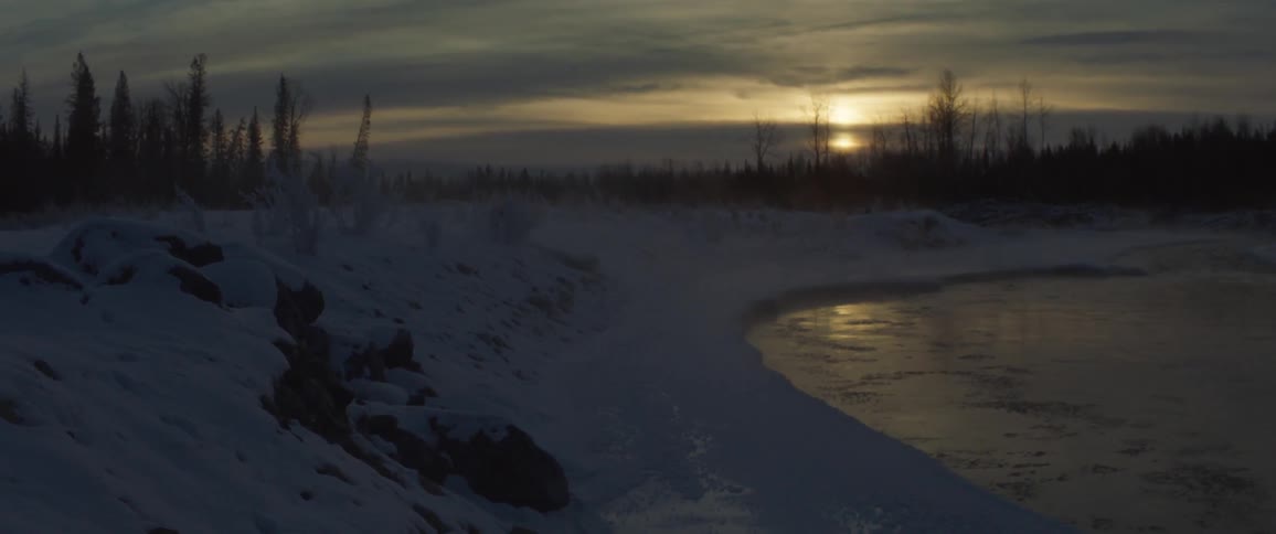 Water is flowing in a river past snow-covered banks at dusk