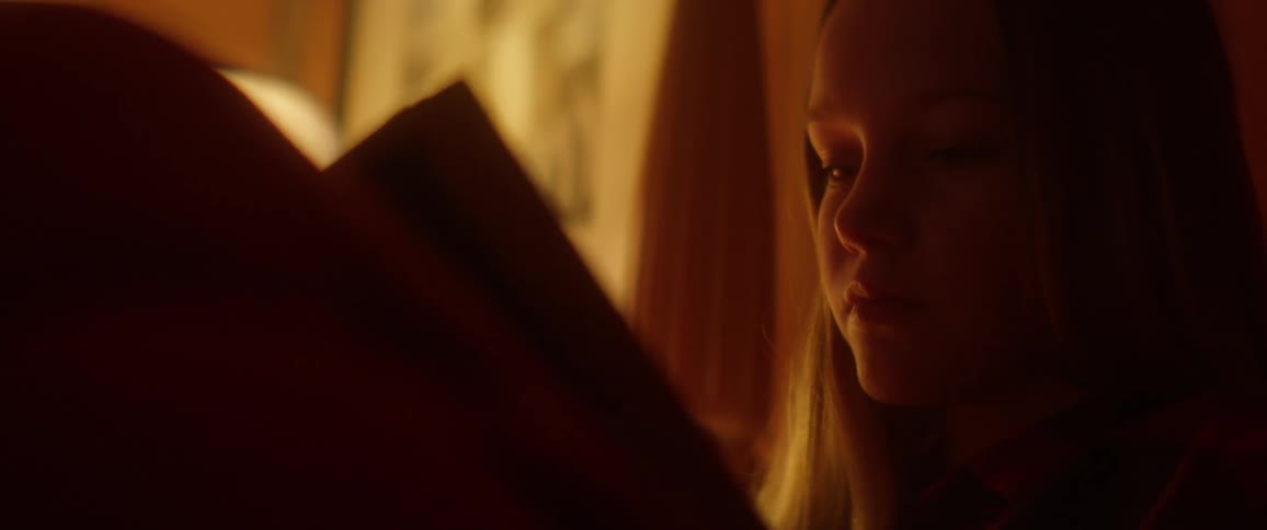 A teenage girl is reading a book in her room at night
