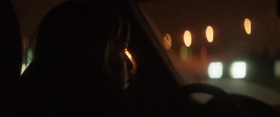 Woman drives a car through a city at night