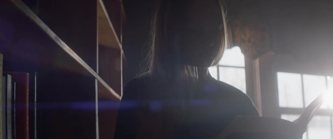 A girl reads a book next to a bookshelf