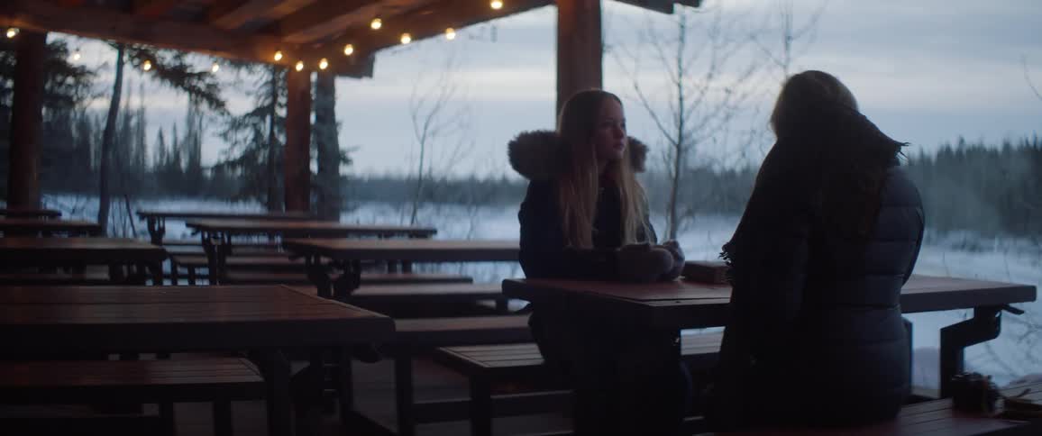 Two women sit at a picnic table in a small pavilion