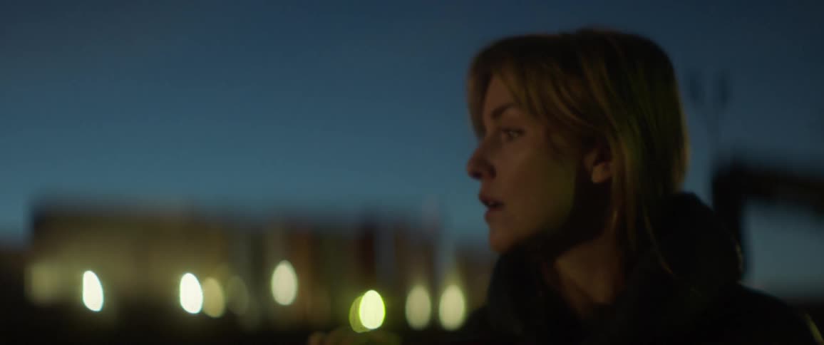 Woman stands outside at sunset with lights behind her