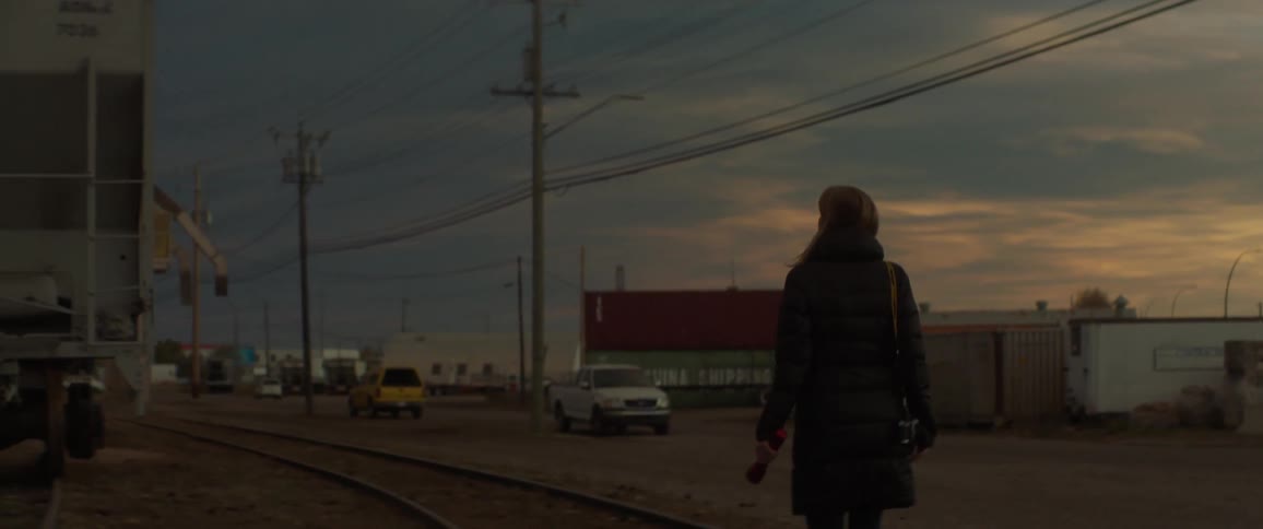 A woman carrying a flashlight is walking along train tracks at dusk