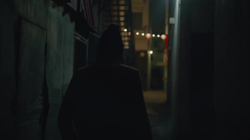 A man wearing a beanie hat smokes as he walks down an alley