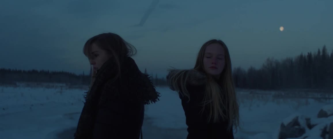 Two girls stand in a snowy field at night