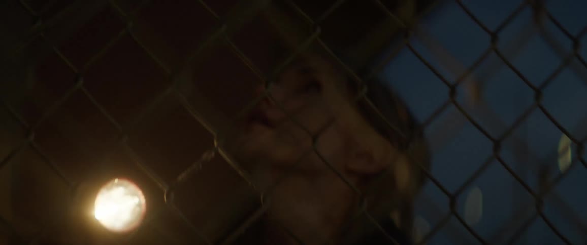 A woman shines a flashlight and yells through a chain link fence