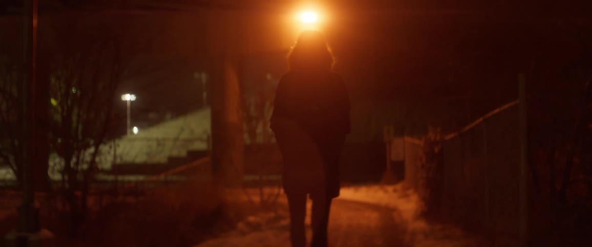 A woman with her coat hood up walks on a path at night