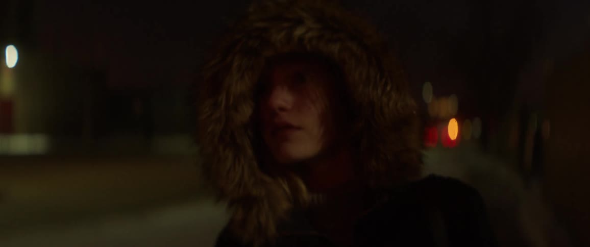 A woman in a large coat walks down the street at night