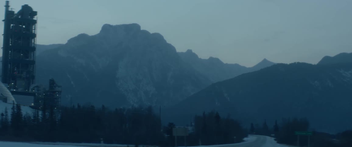 Smoke is rising from an industrial plant in a mountain landscape in winter
