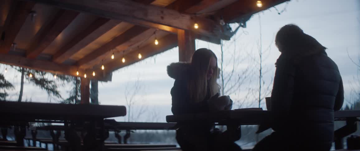 Two women drink coffee at an outdoor table