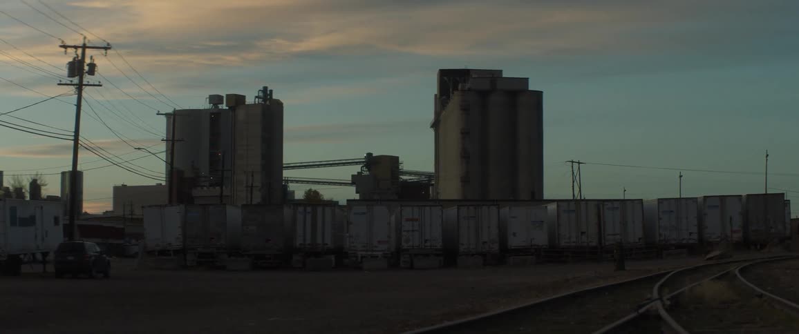 Trailer trucks are parked in a row near an industrial building