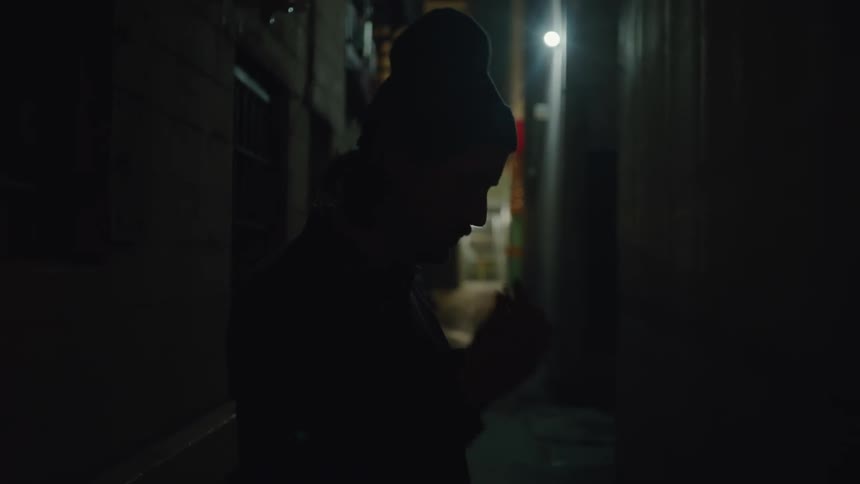 A person is smoking a cigarette in the alley at night