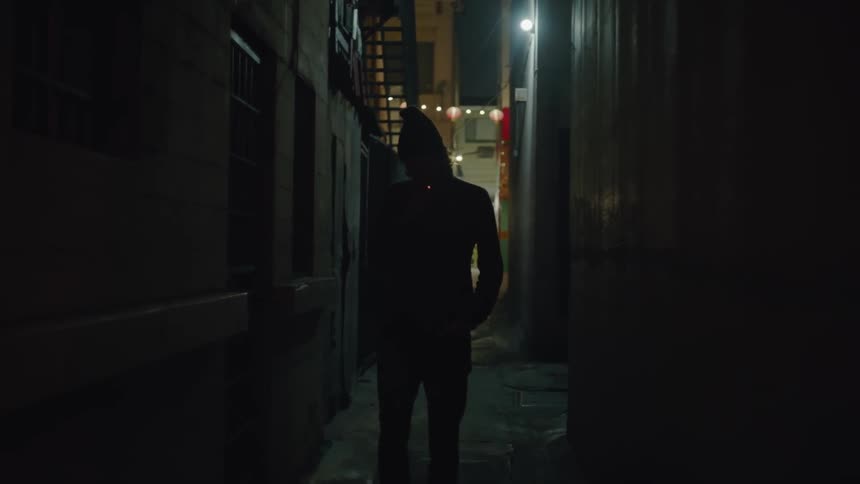A man is walking down a narrow dark alley