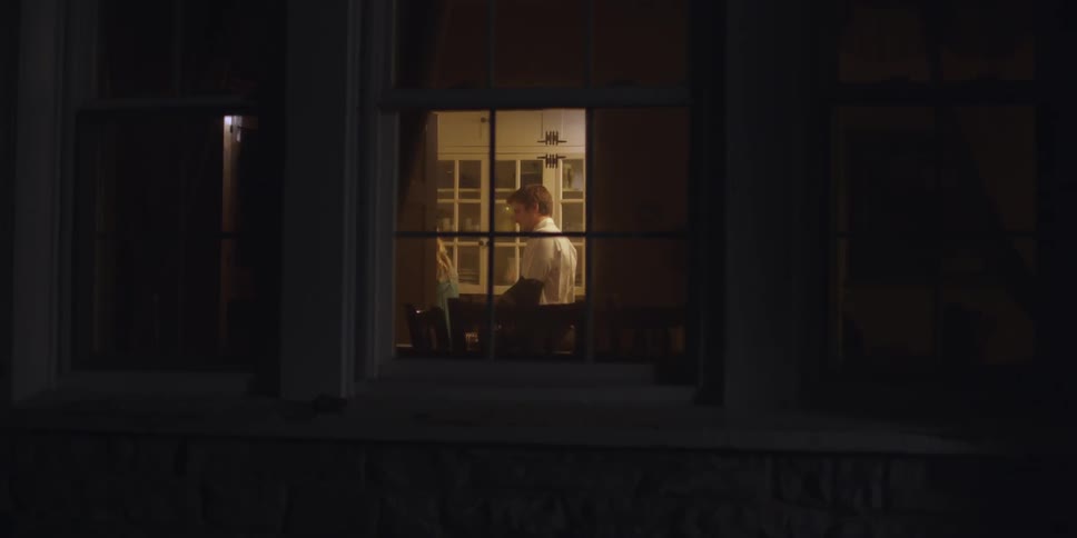 View inside a home from outside of a window as a man walks into a lit room