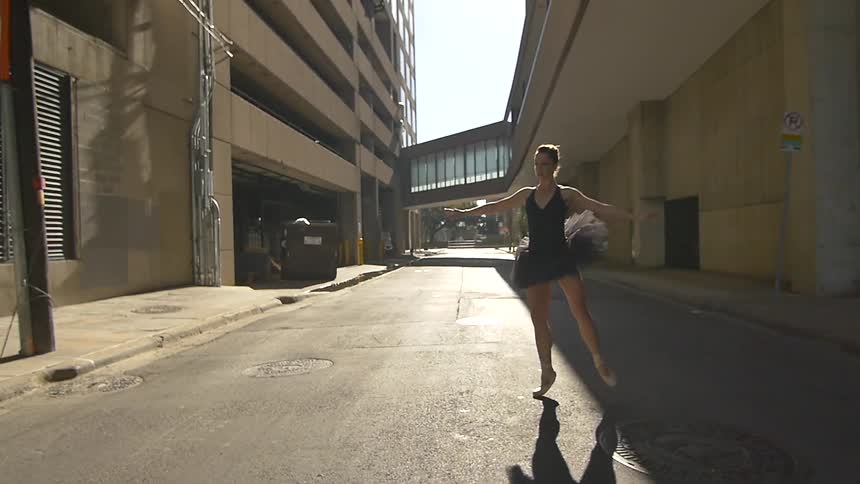 A woman ballet dancing does a jump in the street