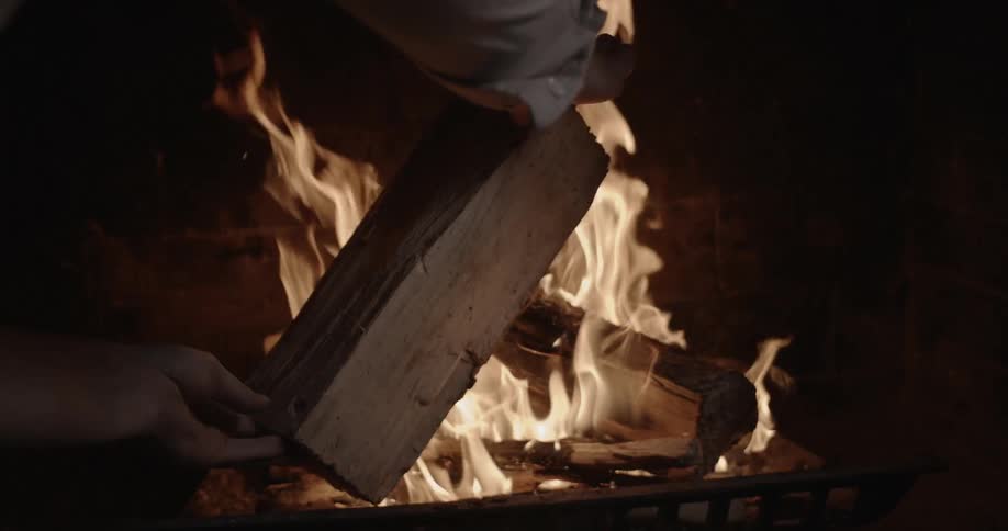 A man is putting a log on a burning fire at night