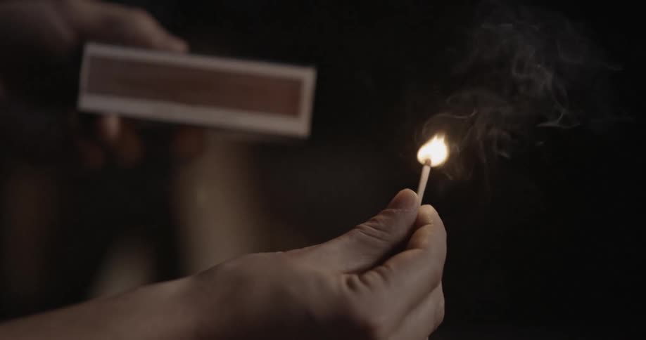 A man strikes a match on the side of a box