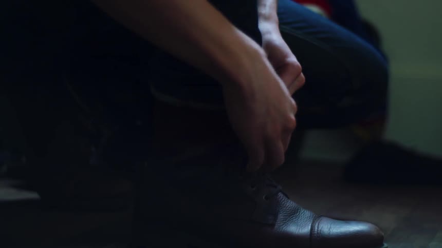 A man is lacing up his boots inside in daylight