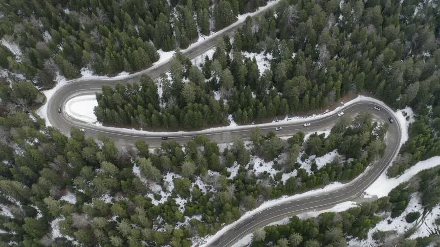 Cars are driving around a winding road in the middle of a snow covered forest