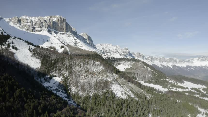A mountain with trees covered in snow is filmed from above