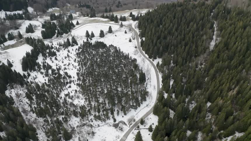 A road is winding through a snow covered tree and valley