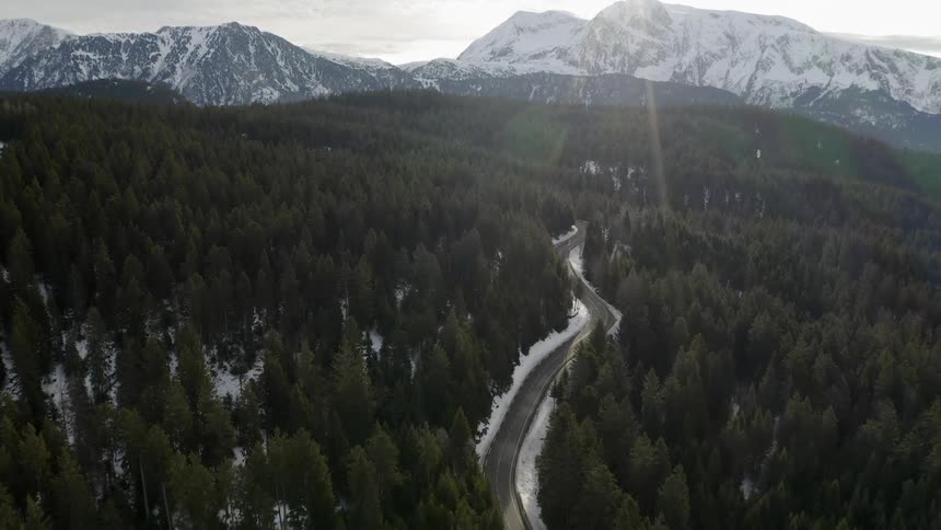 A car travels on a road through the forest and snow