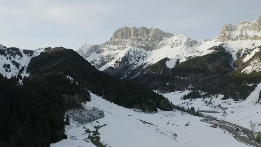 Snow is covering a valley and forest in the mountains on a cloudy day