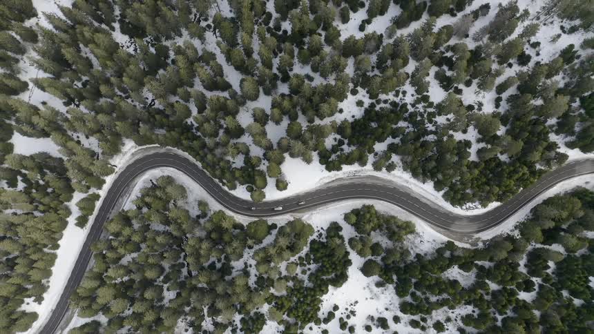 Vehicles are driving on a winding road through a forest on a winter day