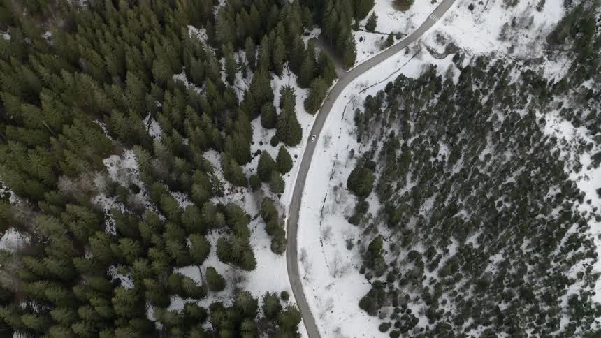 A vehicle is driving on a winding road in a natural landscape in winter