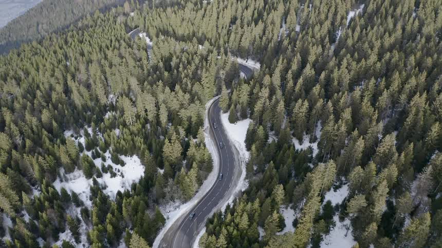 Vehicles are driving on a winding road through a forest on a winter day