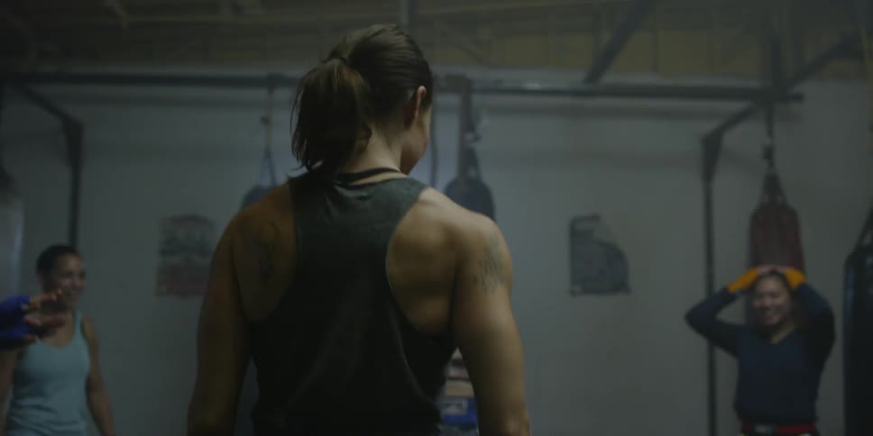 A female athlete is laughing and jogging in place as she trains with others inside a gym