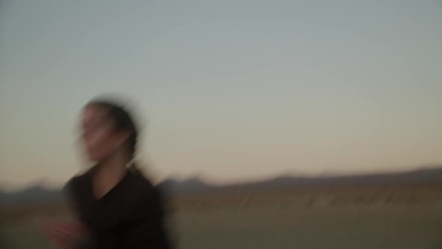 Woman runs on flat dirt land at sunset