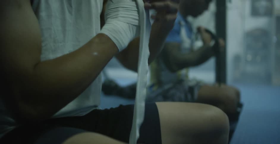 Fighters are sitting in a gym wrapping their hands with tape