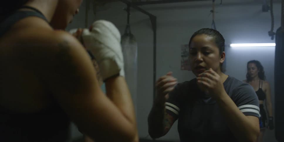 A coach is showing a female fighter how to throw a punch as they train inside a gym