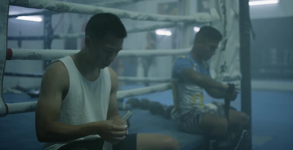 Two fighters are sitting on the edge of a boxing ring taping their hands