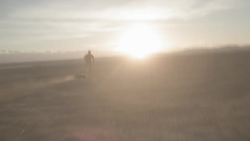 A female athlete is dragging a tire as she runs across a beach in daylight