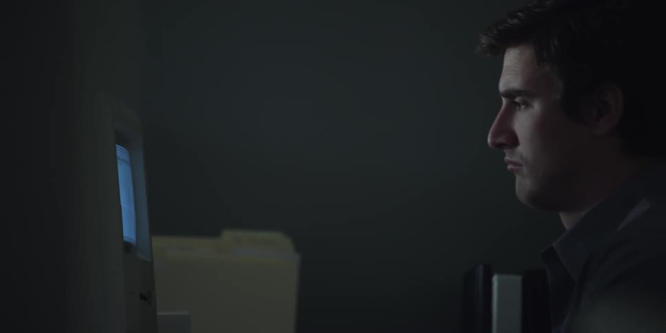 A young man watching a computer monitor in an office