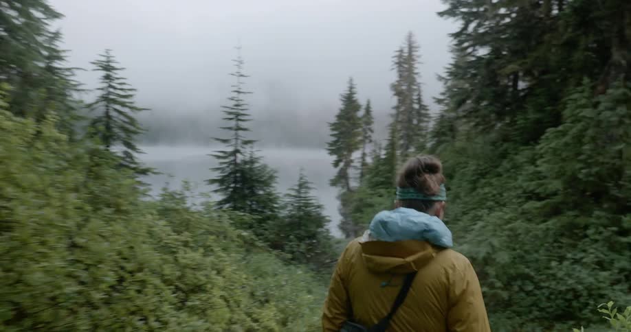 Woman walks through hilly forest towards a lake