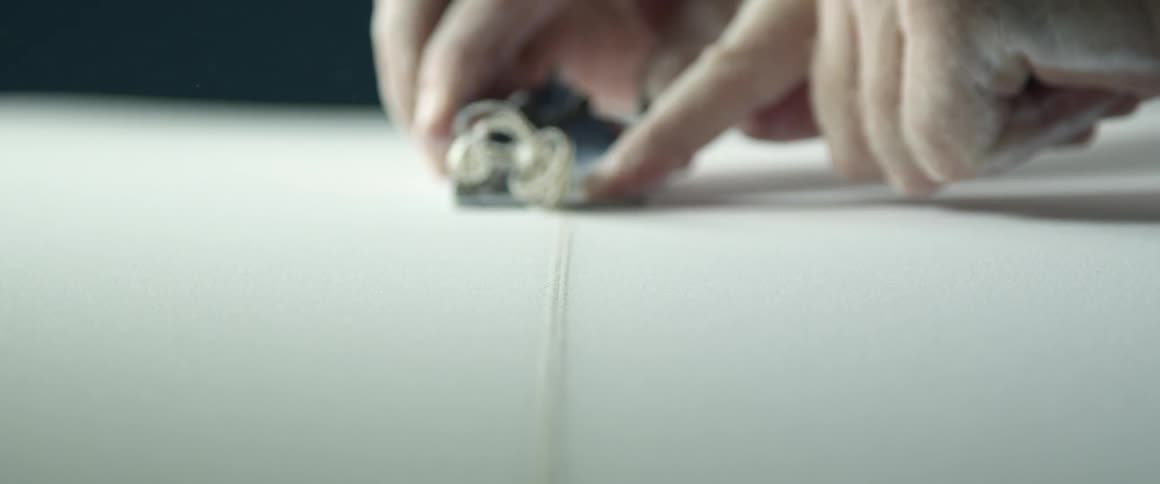 A white man uses a hand tool to shave material off of an object
