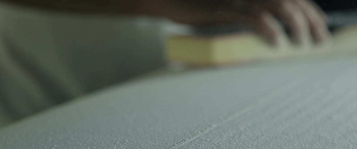 A man is lightly sanding a piece of wood with a sanding block while indoors