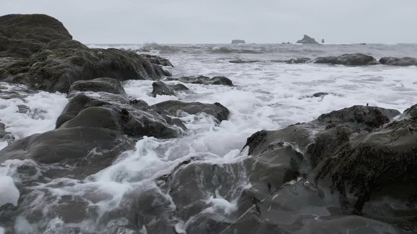 A wave is crashing over rocks and flowing into tide pools on a beach in daylight