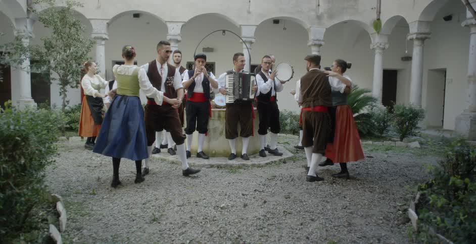 People are in costumes are doing a traditional dance outside in daylight