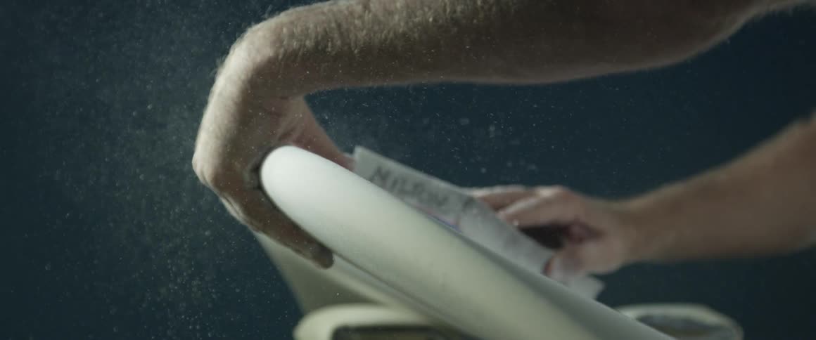 Dust and debris flies around as a man uses a sander on an easel