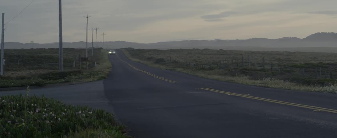 A car drives on a rural road at sunset