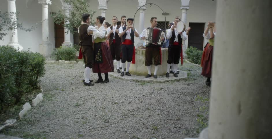 People in costumes are doing a traditional dance outside in daylight