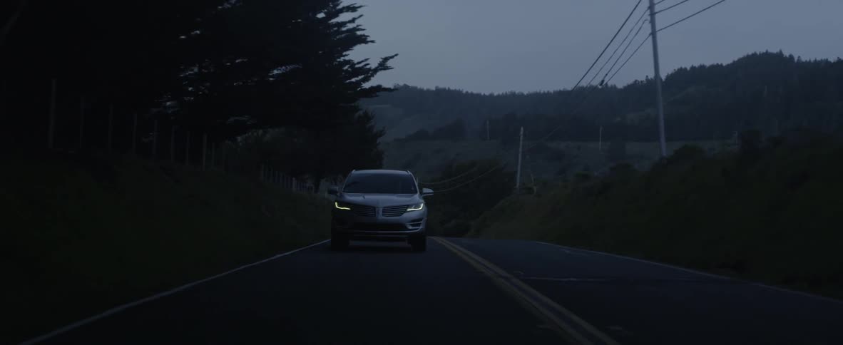 A car drives on a rural road at dusk