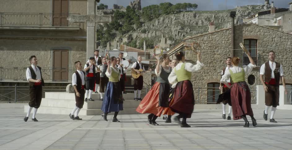 People in costumes are doing a traditional dance outside in daylight